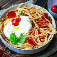 Spaghetti mit Burrata, Kirschtomaten und frischem Basilikum. Cremiger Käse schmilzt auf den Nudeln.