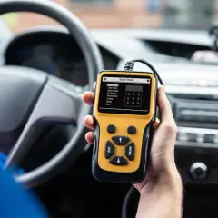 Ręka trzyma żółty skaner diagnostyczny OBD2 w samochodzie, gotowy do porównania z OBD1.