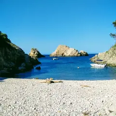 La cala Ferriol, con su playa de guijarros y aguas cristalinas, invita a disfrutar del sol y el mar. Barcas y bañistas comparten este paraíso.
