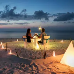 Romantyczna kolacja na plaży. Para świętuje 4 rocznicę ślubu przy blasku lampionów i zachodzącego słońca.