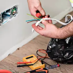 Elektryk przygotowuje przewody. Zielono-żółty kabel to uziemienie, brązowy to faza, a niebieski to przewód neutralny.