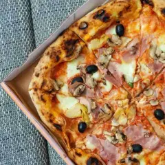 Pyszna pizza capricciosa z szynką, pieczarkami, karczochami i oliwkami w pudełku.