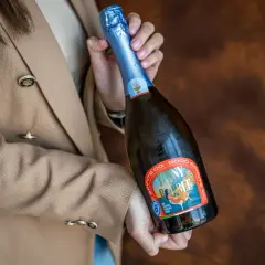 Kobieta w beżowym żakiecie trzyma butelkę musującego napoju, idealnego na międzynarodowy dzień prosecco.
