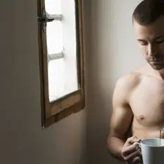 Uomo nudo versa caffè, riflessione sulla psicologia di un uomo sposato. Luce soffusa da una finestra.
