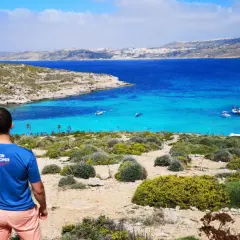 Malta: turkusowa woda, łodzie i skaliste wybrzeże. Widok na zatokę, gdzie widać niewielką ludność korzystającą z uroków wyspy.