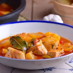 Un plato humeante de patatas con bonito, con trozos de pescado tierno y patatas en una salsa roja sabrosa, adornado con hojas de laurel.