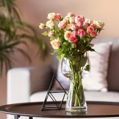 Bukiet róż w wazonie, obok czarny, geometryczny świecznik. W tle sofa i roślina. Do wody z różami warto dodać odżywkę.