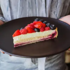 Tranche de tarte aux fruits rouges sur une crème mousseline onctueuse, présentée sur une assiette noire.