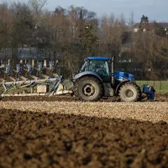 Niebieski traktor z pługiem orze pole. Rolnik przygotowuje ziemię, zastanawiając się, do kiedy można orać pole arimr.