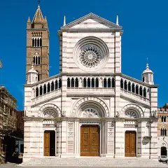 Il Duomo di Grosseto, con la sua facciata a strisce bianche e rosa, domina la piazza. Accanto, un campanile medievale si staglia contro il cielo azzurro.