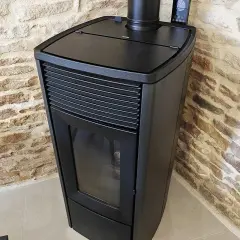 Poêle à granulés noir moderne, avec écran de contrôle, adossé à un mur de pierres. Apprenez comment éteindre un poêle à granulé en toute sécurité.