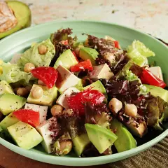 Frischer veganer Salat mit Avocado, Kichererbsen, Tofu und roten Paprikastücken in einer hellgrünen Schüssel.
