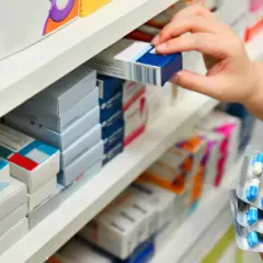 Ręka sięga po lek na półce aptecznej. W dłoni trzyma opakowanie z niebiesko-białymi kapsułkami, zastanawiając się, klacid na co jest stosowany.
