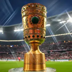 Złoty puchar piłkarski na tle stadionu z widzami i światłami.
