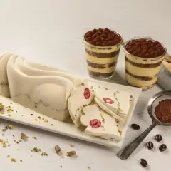 Delikatny krem do tortu z mascarpone, udekorowany malinami i pistacjami, obok deserów tiramisu.