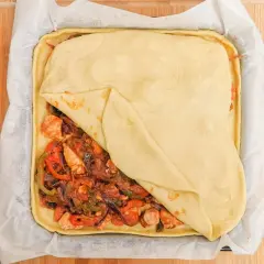 Empanada de pollo lista para hornear, con relleno de pollo y verduras cubierto por masa dorada.