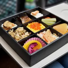 A delicious train bento box filled with various Japanese delicacies, including grilled fish, seafood, and colorful roe, ready for a journey.