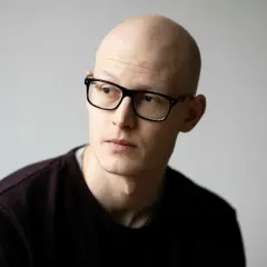 En skallig man med glasögon, Emil Kjær Voss, tittar bortåt med en fundersam blick.
