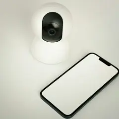 Cámara de seguridad blanca junto a un móvil con pantalla en blanco. Ideal para usar móvil viejo como cámara de seguridad.