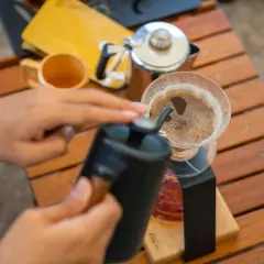 Ręce przygotowują aromatyczną kawę w górach. Ciepły napój parzy się w dripperze, a obok stoi kubek.
