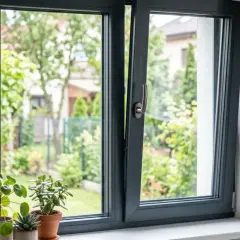 Nowoczesne, ciemnoszare okno z widokiem na zielony ogród i rośliny na parapecie.