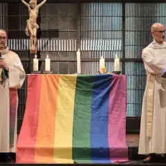 Zwei Geistliche mit Regenbogenfahne und Kreuz im Hintergrund. Ein Gottesdienst für die gleichgeschlechtliche Ehe in der Kirche.