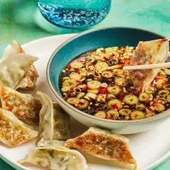 A gyoza is dipped into a flavorful gyoza dipping sauce with scallions and chili flakes.
