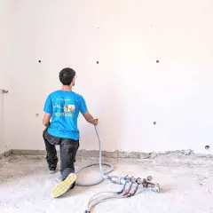 Operaio in ginocchio esegue coibentazione pareti con insufflaggio. Attrezzatura per isolamento termico a terra.