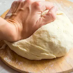 Main d'une personne pétrissant une pâte à pain sur une planche en bois. Une question se pose : pourquoi ma pâte ne lève pas ?