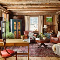 Rustic living room with wooden beams, leather armchairs, a patterned rug, and a vintage cabinet.