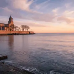 Edificio histórico junto al mar al amanecer, evocando poemas del mar.