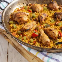 Paella de pollo recién hecha, con trozos dorados de pollo, arroz amarillo y verduras.