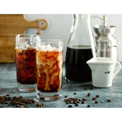 Dwa szklanki orzeźwiającego cold brew z lodem i mlekiem, obok dzbanek z kawą i młynek. Idealne na gorące dni, przygotowane z myślą o miłośnikach kawy.