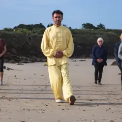 Un groupe suit un homme en tenue jaune lors d'une marche afghane sur une plage.