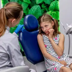 Dziewczynka z niepokojem czeka na usunięcie zęba, podczas gdy dentystka w rękawiczkach przygotowuje się do zabiegu.
