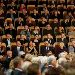 Elegancko ubrani widzowie siedzą w teatrze, gotowi na spektakl. To inspiracja, jak się ubrać do teatru.