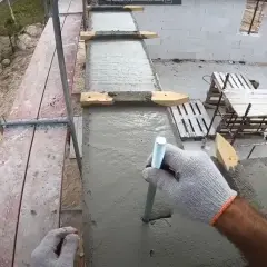 Ręka w rękawicy wkręca pręt w świeży beton. To mocowanie murłaty bez wieńca, kluczowe dla stabilności konstrukcji.