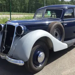 En mörkblå Horsch bil från 1930-talet, med reservhjul monterat på sidan, står parkerad utomhus.