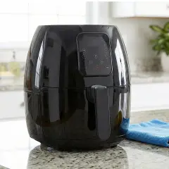 Friggitrice ad olio nera lucida con pannello digitale, accanto a limoni e un panno blu. Ideale per imparare come pulire la friggitrice ad olio.