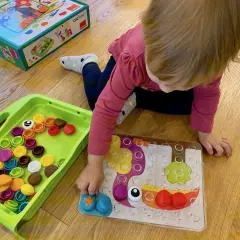 Mała dziewczynka układa kolorowe koraliki na tablicy. Idealna zabawa co dla dwulatka, rozwijająca kreatywność i zdolności manualne.