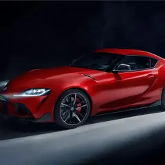 Un deportivo Toyota Supra rojo brillante, con luces encendidas y humo detrás, listo para la acción.