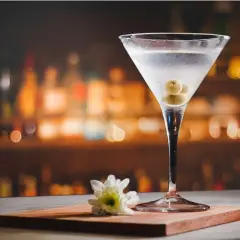 Kryształowy kieliszek z martini, ozdobiony oliwkami, na tle rozmytego baru. Idealny drink, by poczuć smak elegancji.