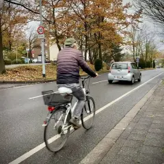 Mann fährt Rad auf einem geschützten Radweg. Ein Auto fährt auf der Straße.