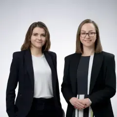 Dwie kobiety w garniturach, prawniczki, na jasnym tle.