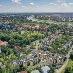 Nowoczesne osiedle w otoczeniu zieleni, z widokiem na rzekę i miasto. W oddali widać zabytkowe budynki i nowe apartamentowce. To idealne miejsce dla osób ceniących spokój i bliskość natury, a jednocześnie dostęp do miejskich atrakcji.