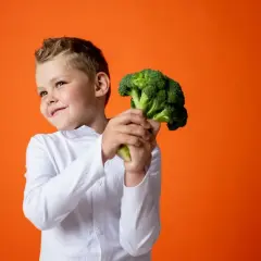 Bambino sorridente con un broccolo, un ortaggio salutare. Non è un legume, ma è ottimo per la salute!