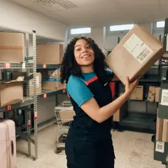 Lächelnde Frau mit Paket in einem Lager, bereit für den Versand. Alle Zollformalitäten sind erledigt.