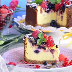 Pyszny sernik z owocami leśnymi, udekorowany malinami i porzeczkami, kusi swoim wyglądem.