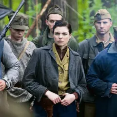 Grupa żołnierzy w lesie, w tym kobieta z pistoletem przy pasie. W tle widać broń maszynową. To scena z filmu "Czas honoru".