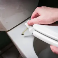 Dłoń montuje zawias deski wolnoopadającej. Naprawa deski wolnoopadającej zakończona sukcesem.